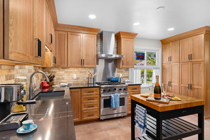 A view of a renovated kitchen with a black island in the foreground and a professional-grade stove in the background.